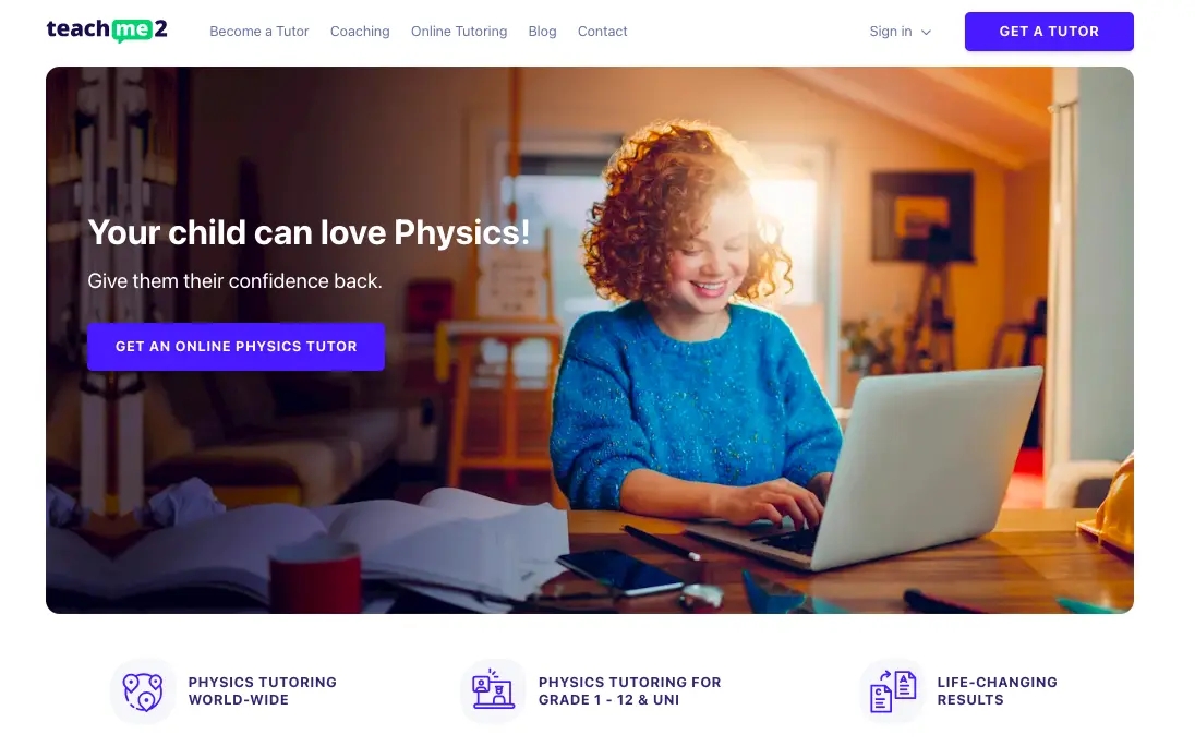 Child smiling while using a laptop for online physics tutoring at home with study materials on desk